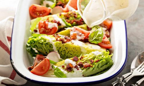 Wedge salad with baby lettuce, cherry tomatoes, bacon and ranch dressing pouring over