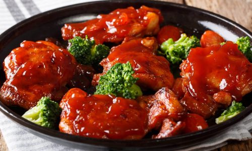 Delicious glazed chicken with spicy sauce and tomatoes, broccoli close-up on a plate. horizontal